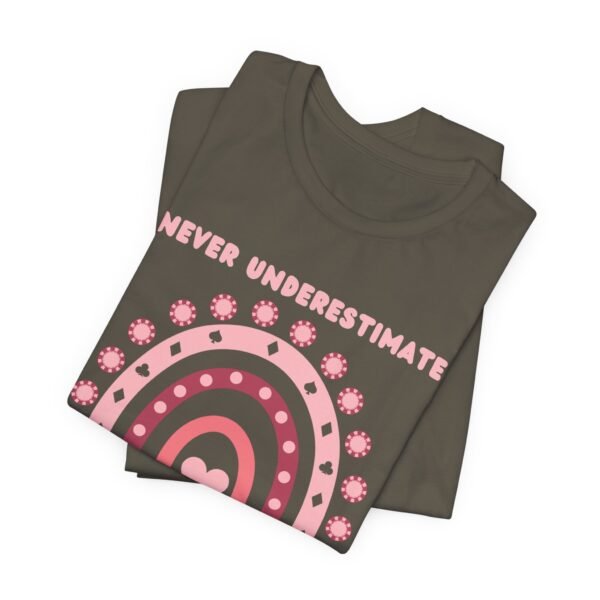 A folded army colored Bella+Canvas 3001 T-shirt featuring a boho rainbow graphic in shades of pink. The graphic incorporates elements of the game of poker, such as card suits and poker chips. The text in the design says "Never underestimate a girl who plays poker".