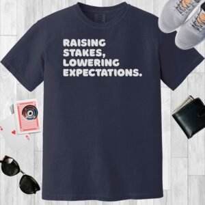 Navy colored unisex crewneck poker-themed T-shirt. Design features the text 'Raising stakes, lowering expectations.'