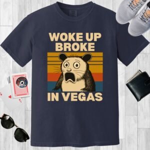 Navy colored unisex crewneck poker-themed T-shirt. Design features the text 'Woke up broke in Vegas'. Image of a stunned possum on a sunset background.