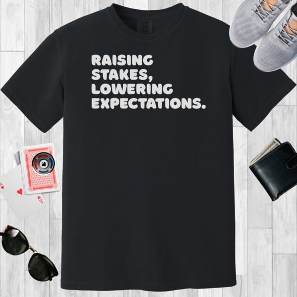 Black colored unisex crewneck poker-themed T-shirt. Design features the text 'Raising stakes, lowering expectations.'