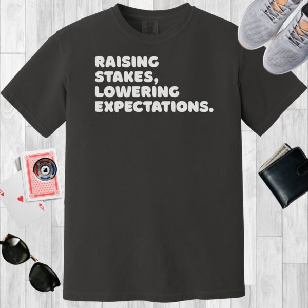 Graphite colored unisex crewneck poker-themed T-shirt. Design features the text 'Raising stakes, lowering expectations.'