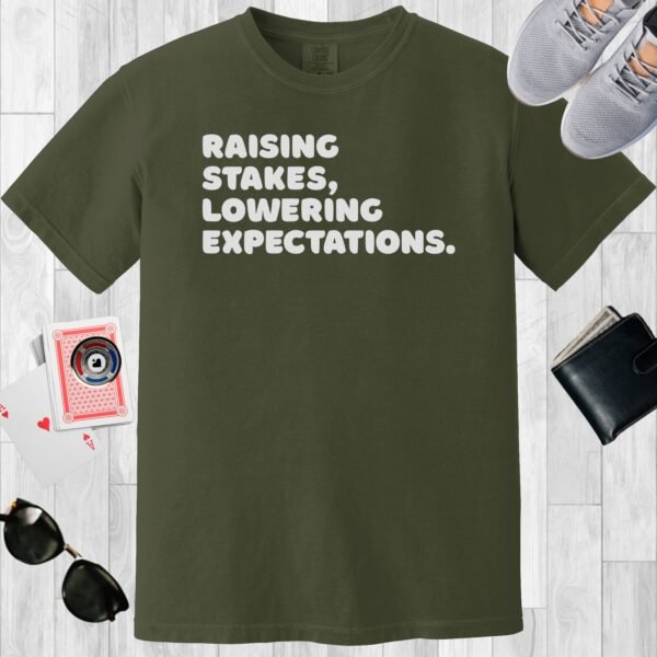 Moss colored unisex crewneck poker-themed T-shirt. Design features the text 'Raising stakes, lowering expectations.'