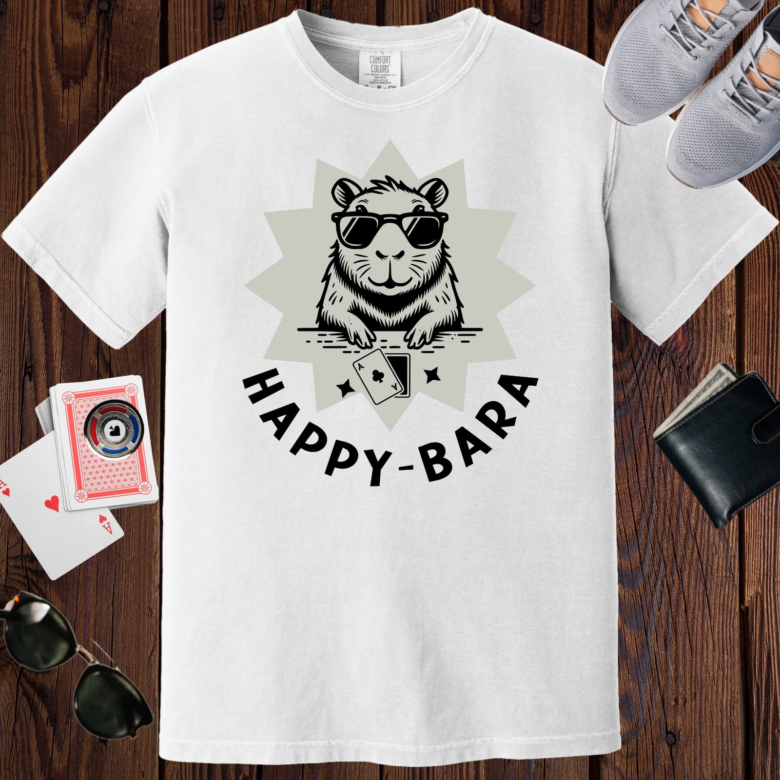 White colored unisex crewneck poker-themed T-shirt. Design features the text 'Happy-bara'. An image of a sunglass-wearing capybara with playing cards on a starburst background.